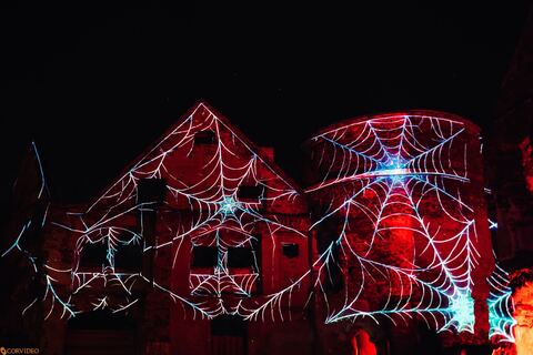 Mapping świecących pajęczyn na murach i wieży zamku nocą
